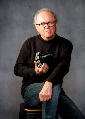 Der Fotograf Franz Bauer, eine schwarze Kamera in der Hand haltend