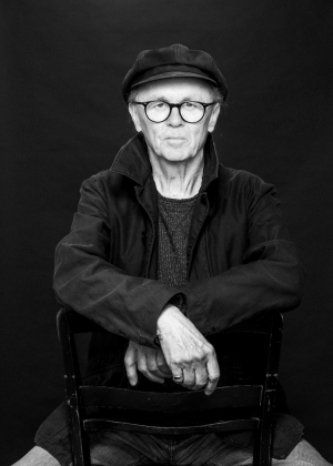 Der Fotograf Franz Bauer, eine schwarze Kamera in der Hand haltend